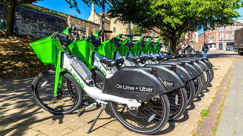 Seven electric Lime e-bikes parked neatly on a pavement in Nottingham with views of Nottingham Castle in the background