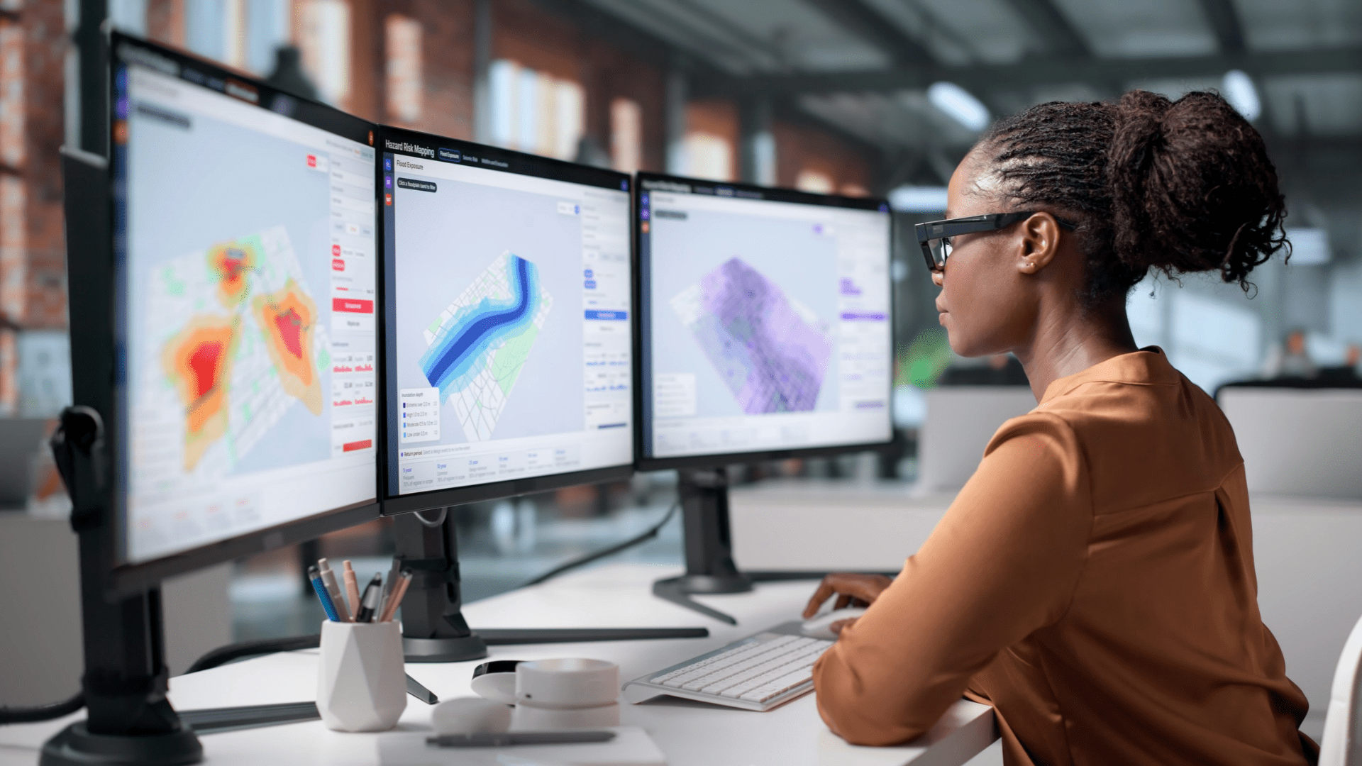 Professional analysing digital mapping and planning data across multiple computer screens in an office environment.