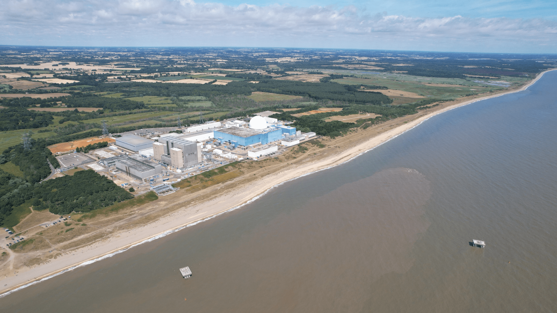 Aerial view of a large coastal energy facility located beside a shoreline and surrounding countryside.