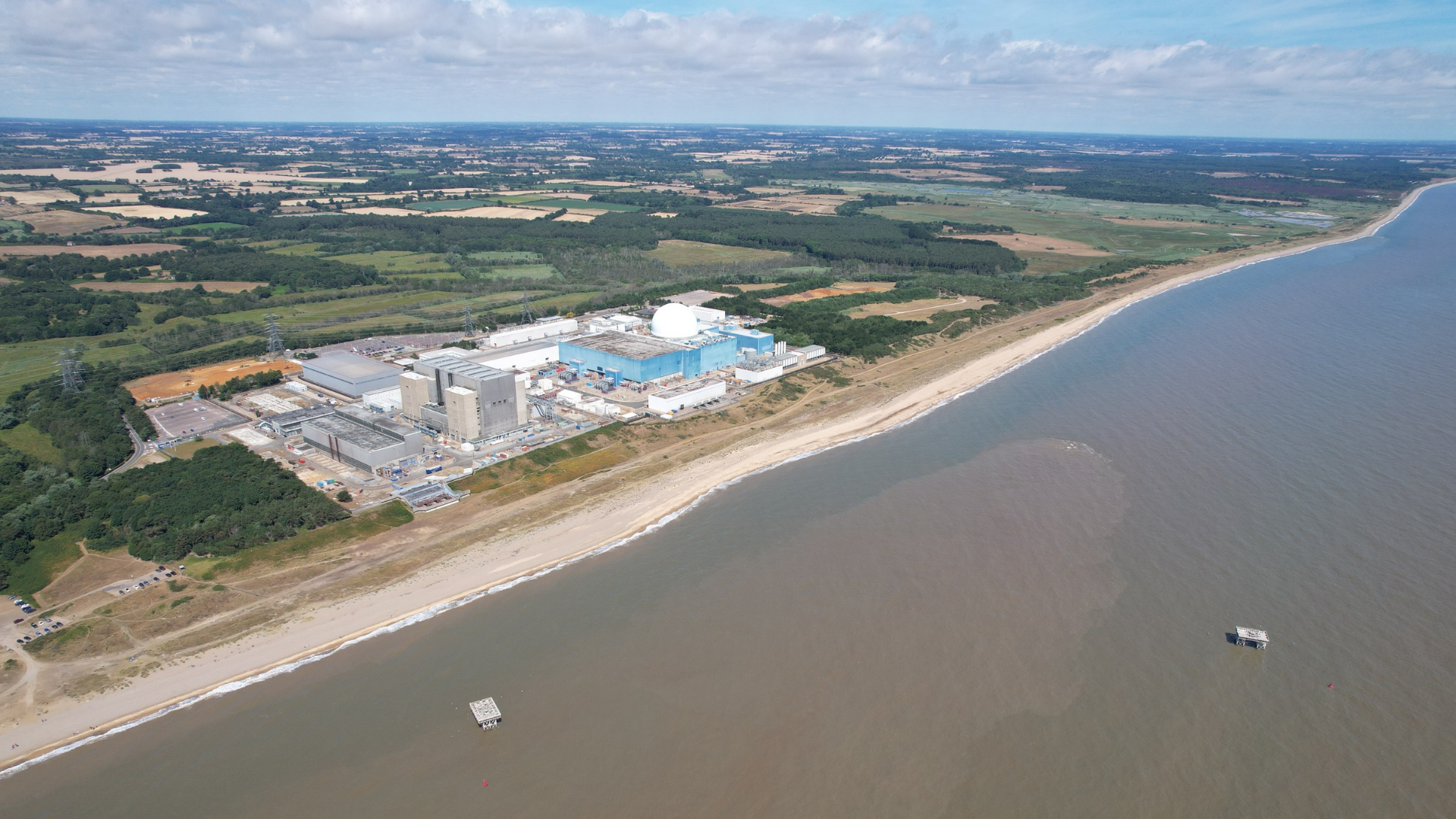 Aerial view of a large coastal energy facility located beside a shoreline and surrounding countryside.