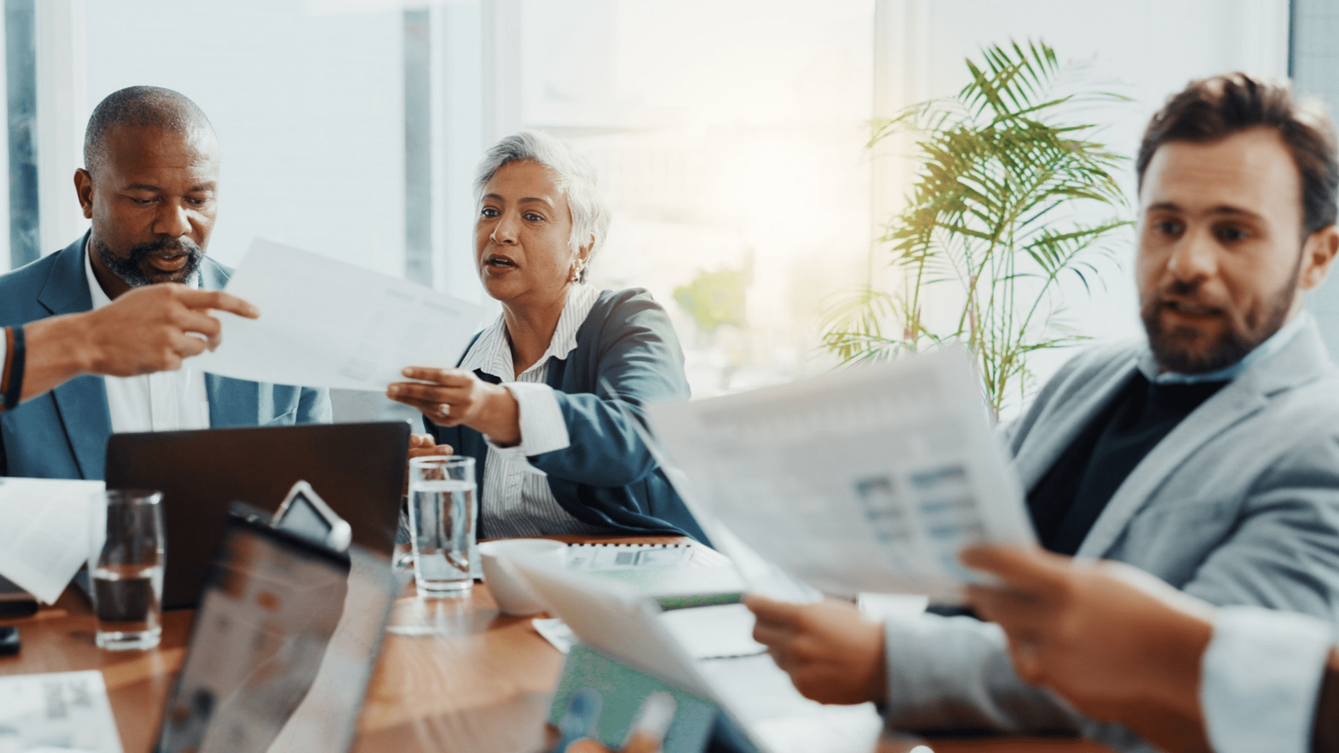 Professionals exchanging documents and reviewing reports during a business meeting in a conference room.