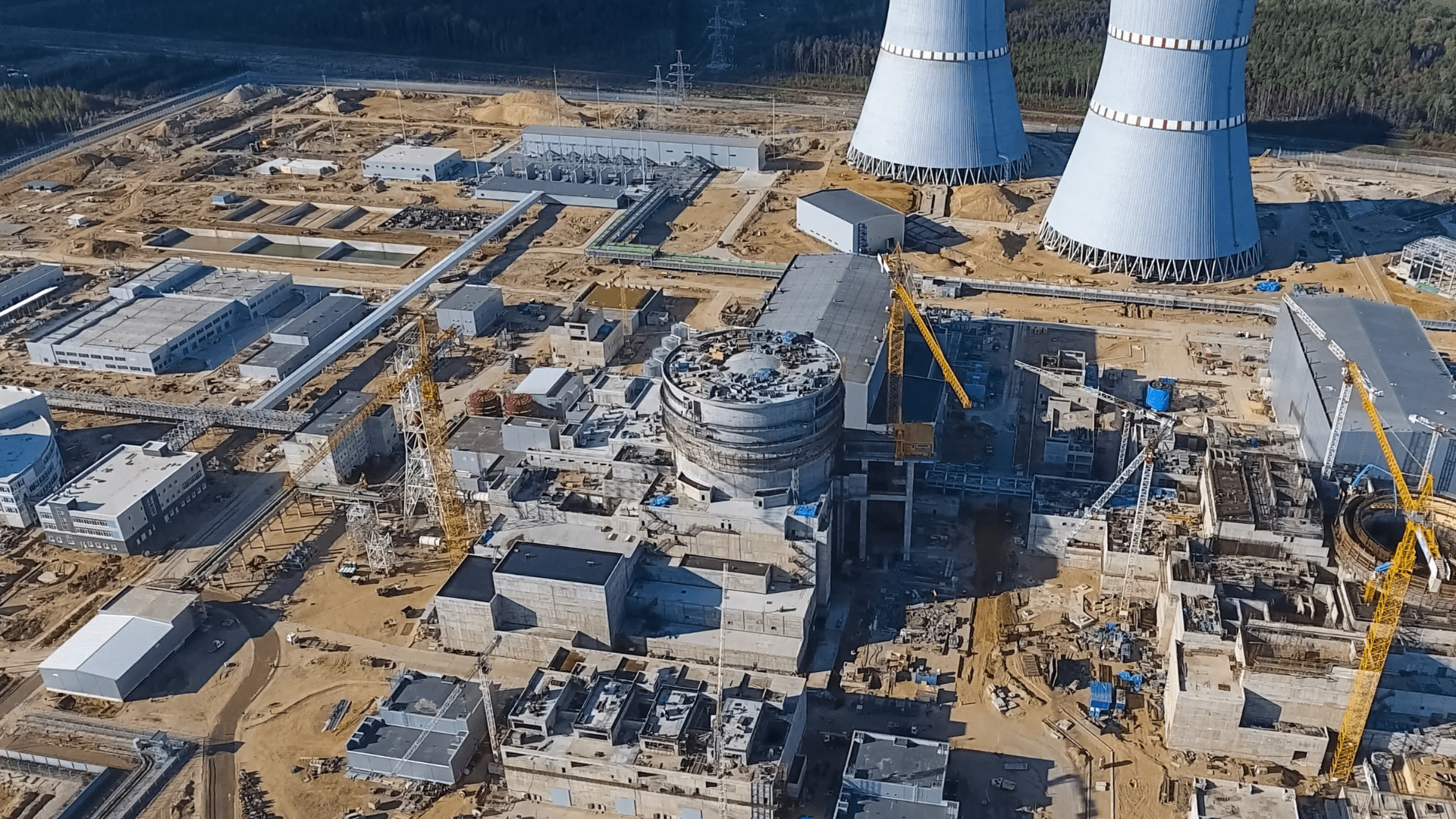 Aerial view of a large energy infrastructure construction site with cooling towers, industrial buildings and cranes.