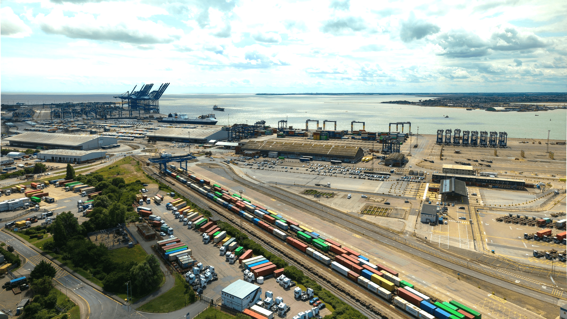 Aerial view of a major port and logistics hub featuring container terminals, rail freight infrastructure, warehouses and waterfront shipping operations.