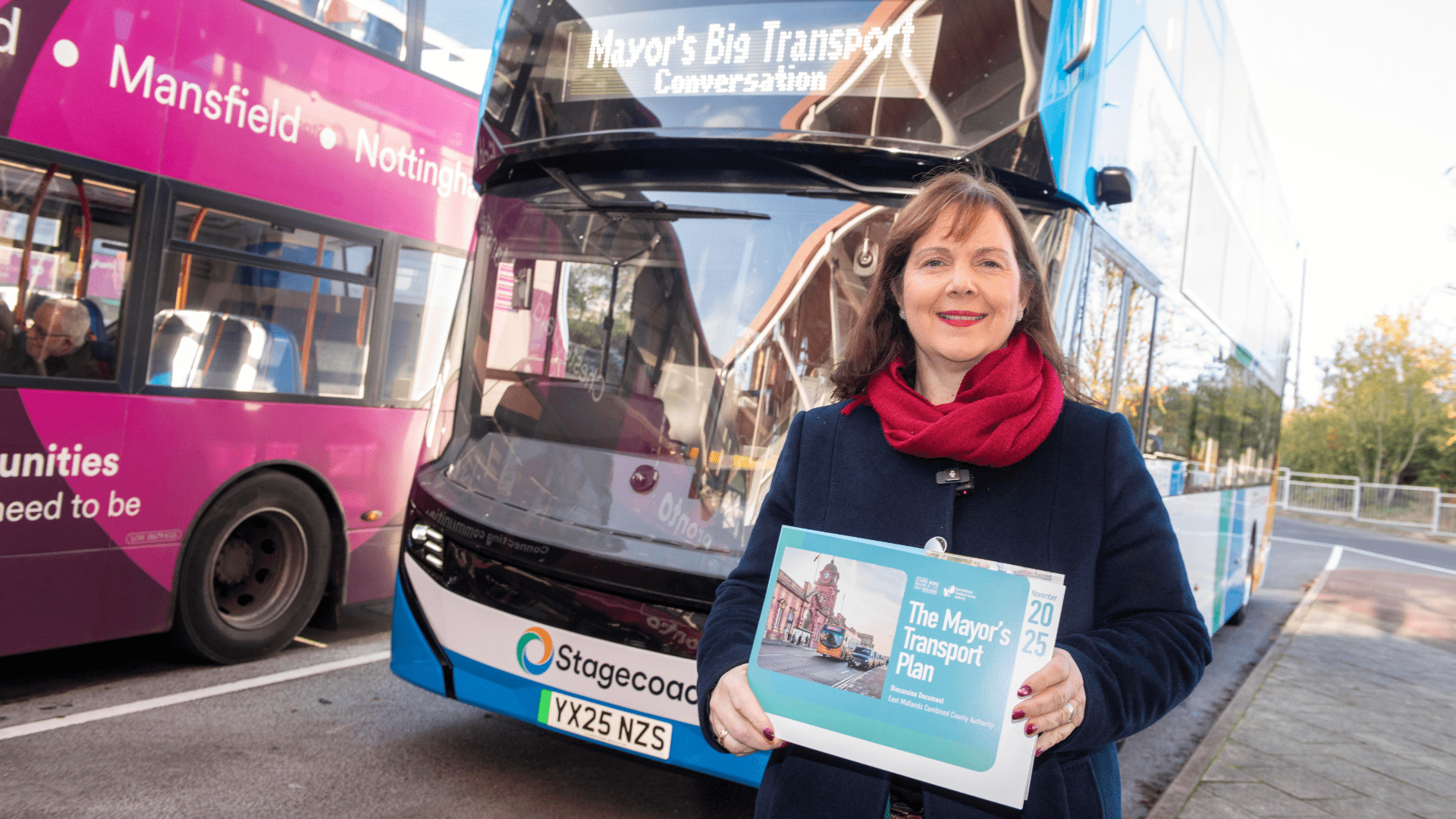 The Mayor is sat on a bus, smiling, reading a Transport Plan brochure